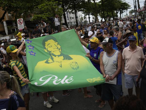 Menschen halten ein Banner des verstorbenen brasilianischen Fußballstars Pele entlang der Route seines Trauerzuges. 