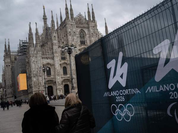 People walk past fences displaying the logo of Milano Cortina 2026 Olympic Games in Duomo’s square, in Milan on January 27, 2026. (Photo by MARCO BERTORELLO / AFP)
