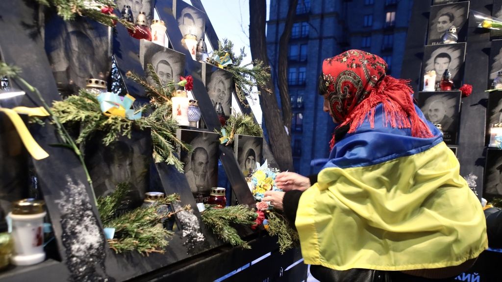 Eine Frau, die in eine ukrainische Flagge gehüllt ist, stellt Blumen und eine Kerze vor das Foto eines Gefallenen am Ehrentag der Hundert Himmlischen Helden. (Foto)